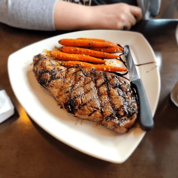 Dunmire's on the Lakes' grilled steak with roasted carrots and a knife on a white plate.