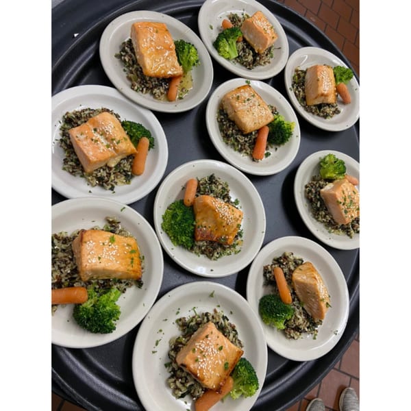 Multiple plates of Dunmire's on the Lakes salmon with wild rice, broccoli, and carrots on a tray.