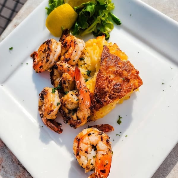 Grilled shrimp with a side of cheesy potatoes, lemon wedges, and a small green salad.