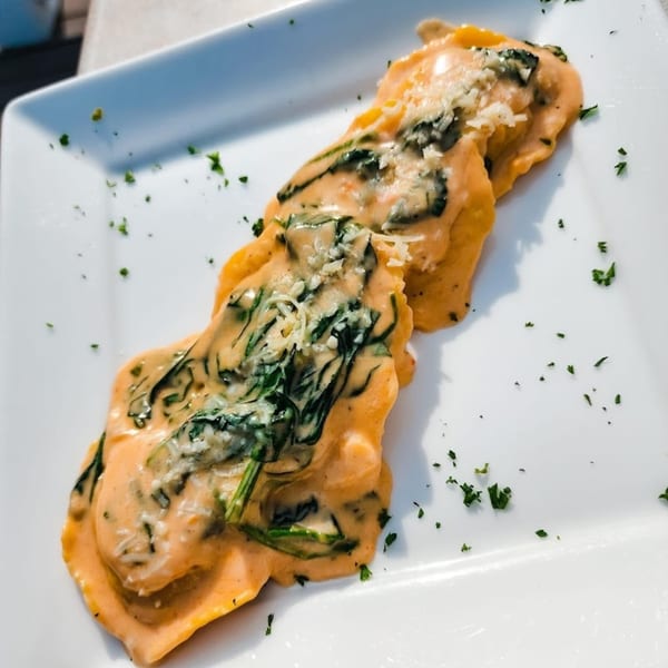 Dunmire's on the Lakes' ravioli with creamy sauce, spinach, and grated cheese on a white plate.